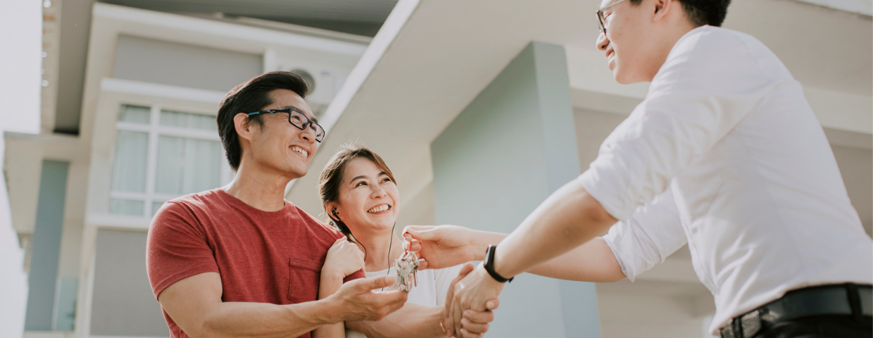 A real estate agent hands the keys to a new home to a man and woman.