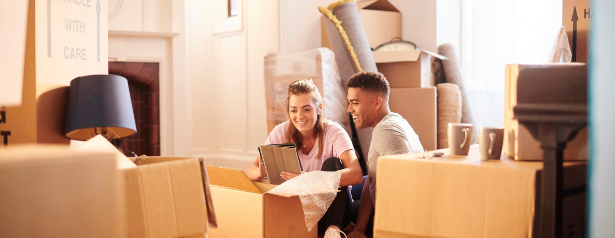 A man and a woman sit in their home among a pile of boxes.