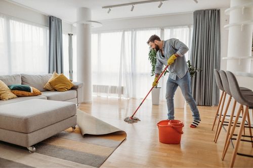 A man wearing rubber gloves mops his hardwood floor in his living room