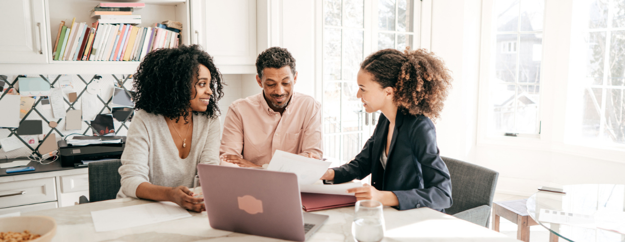 A man and a woman and their insurance agent sit at a table and review insurance paperwork.