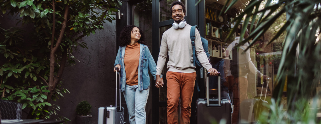 A Black heterosexual couple leaves their vacation rental with suitcases in hand, from the additional dwelling unit they stayed in with its own entrance.