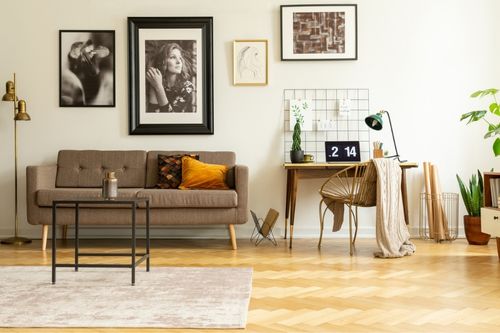 A young man relaxes in the living room of his rental looking out his window with beige curtains and house plants around him