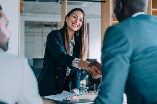 A female real estate agent shakes hands with her client at a conference table