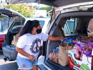 A woman unpacks food donations from the back of a vehicle.