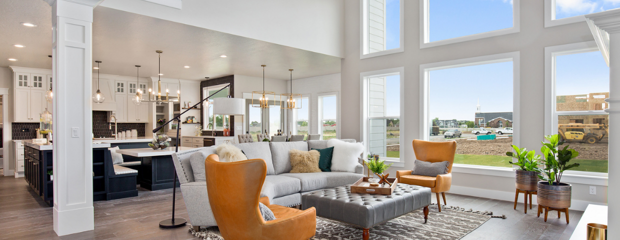 A large, open living room and kitchen area decorated with modern furniture, house plants, and exposed light fixtures.