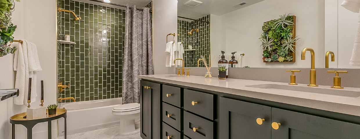 A bathroom with dark green cabinets, green shower tiles, and gold fixtures.