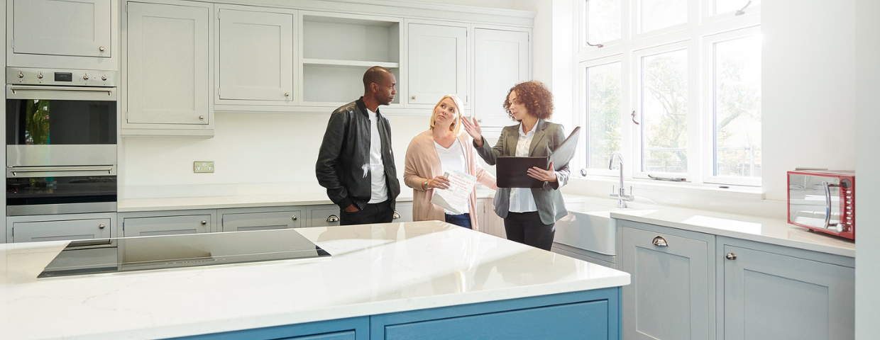 A real estate agent shows a kitchen to a man and a woman.