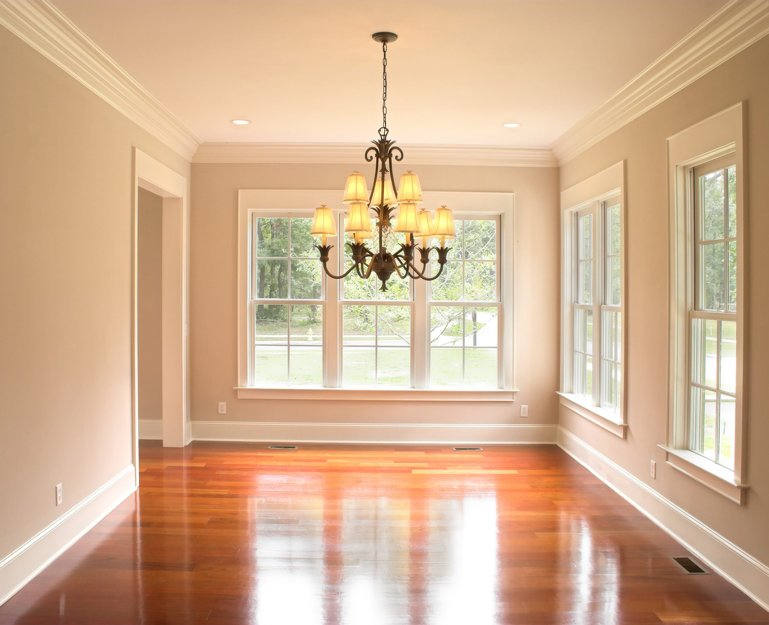 An empty living room with a chandelier, crown molding, and a hardwood floor.