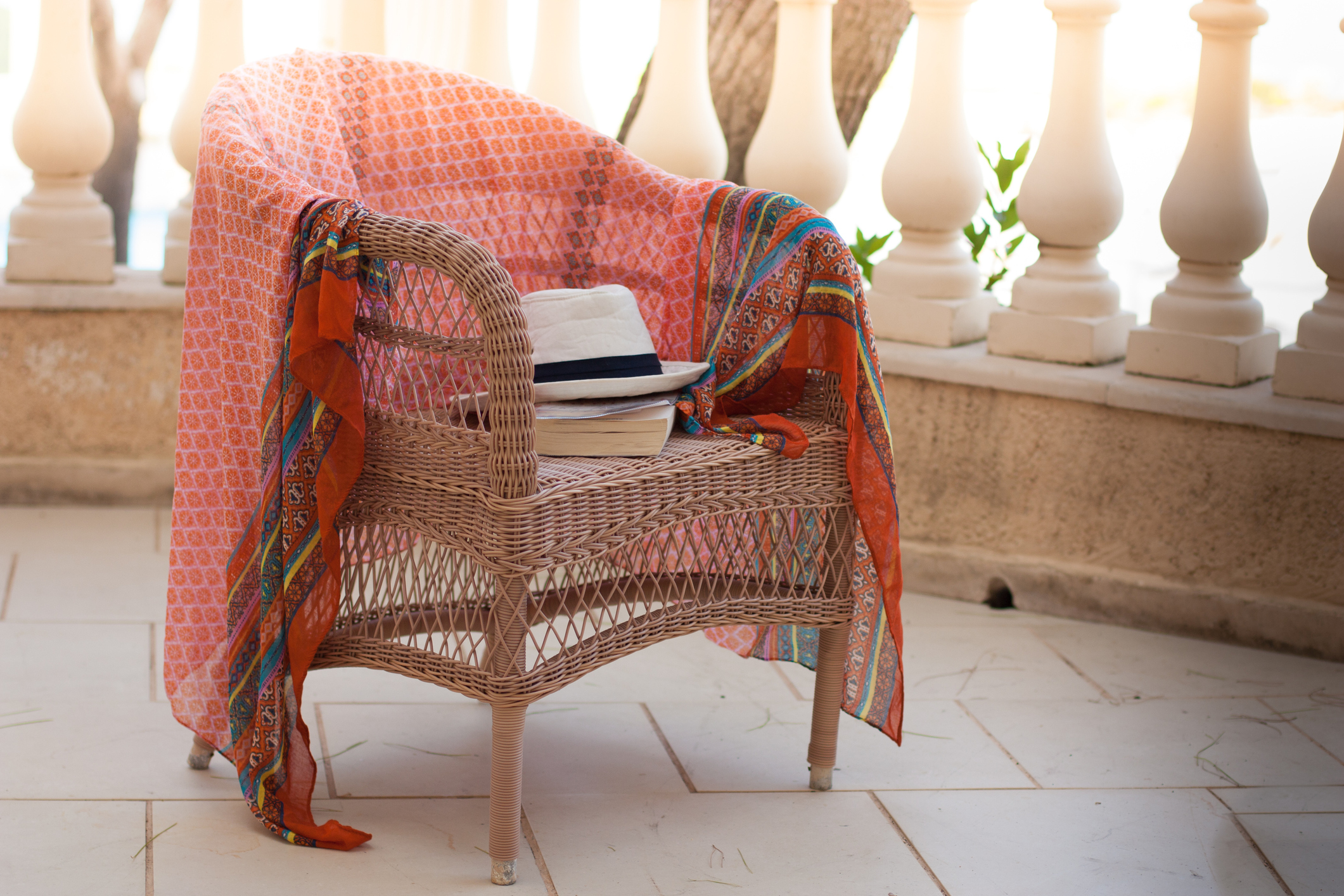 A wicker chair holding a book, a hat, and a blanket.