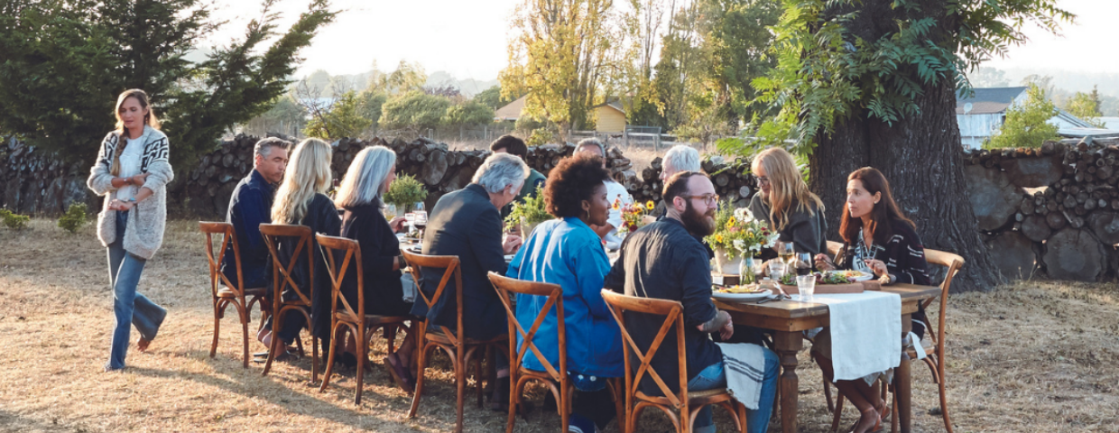 A group of people sit around a large table at a backyard party.