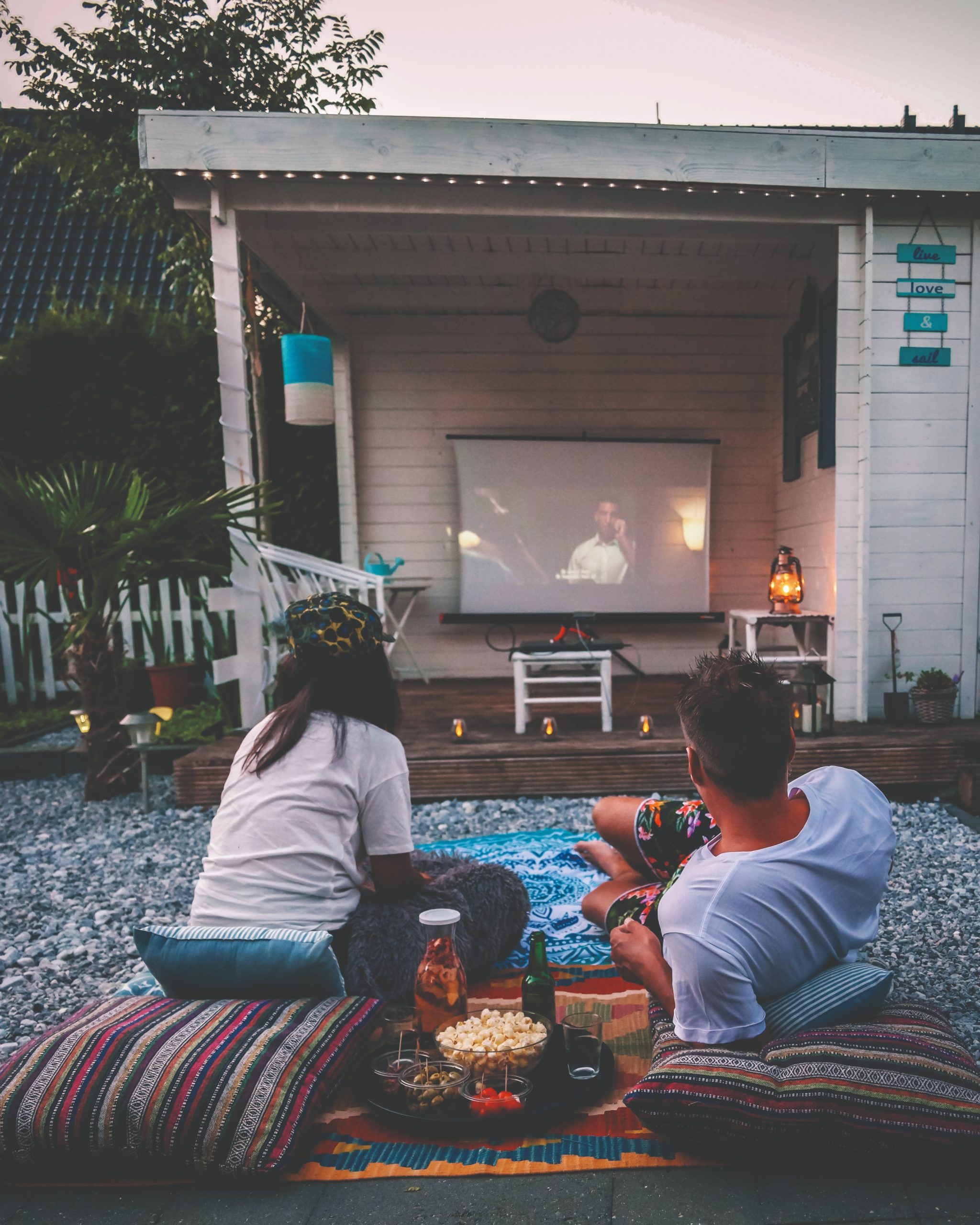 A man and a woman watch a movie on a projector from their driveway.
