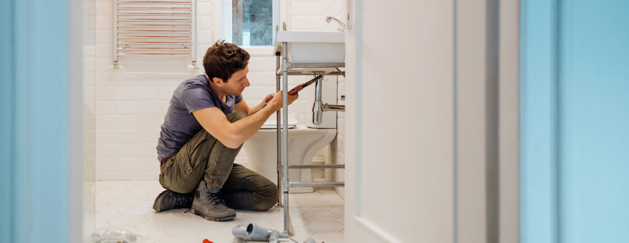 A man repairs the plumbing in his bathroom.