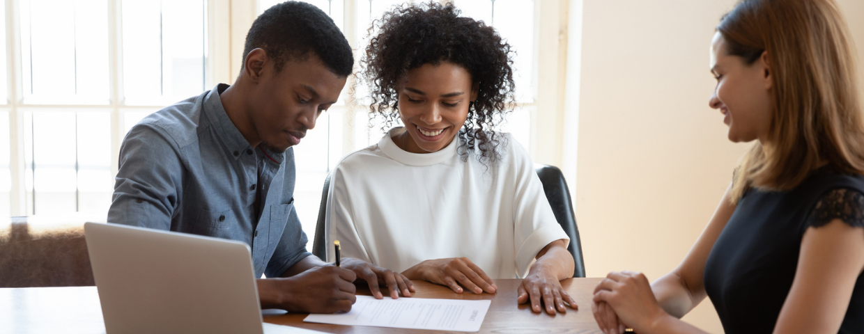 A young man and woman sign a contract as their real estate agent looks on.