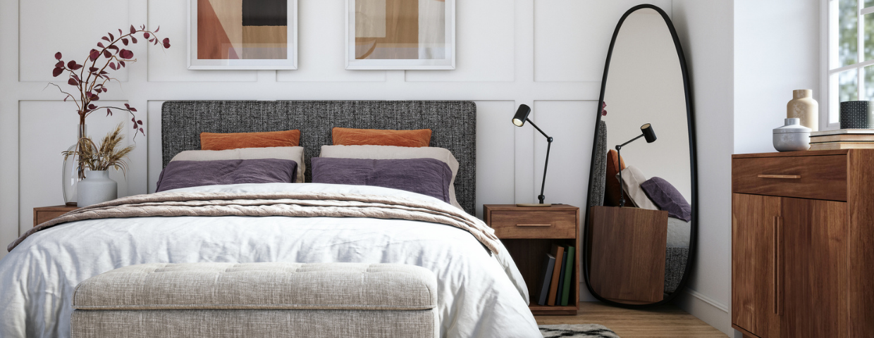 A bedroom with an oval mirror in the corner, geometric drawings on the wall, a wooden nightstand and dresser.