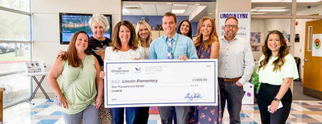 A group of people inside a school hold up a check for one-thousand dollars.