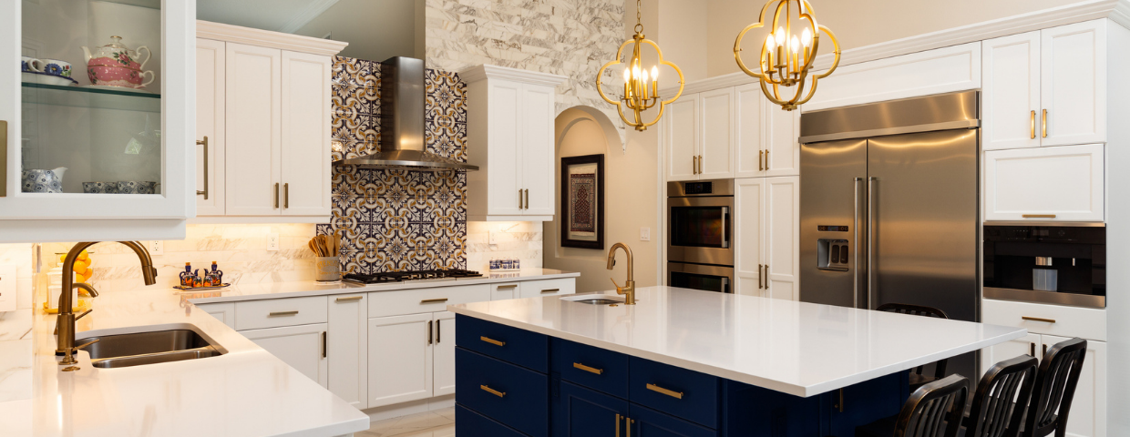 A kitchen with white surfaces, decorative tile, a blue island, and gold light fixtures.