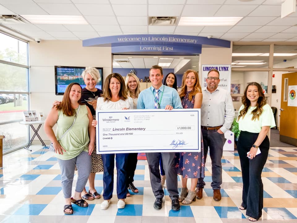 A group of people inside a school hold up a check for one-thousand dollars.
