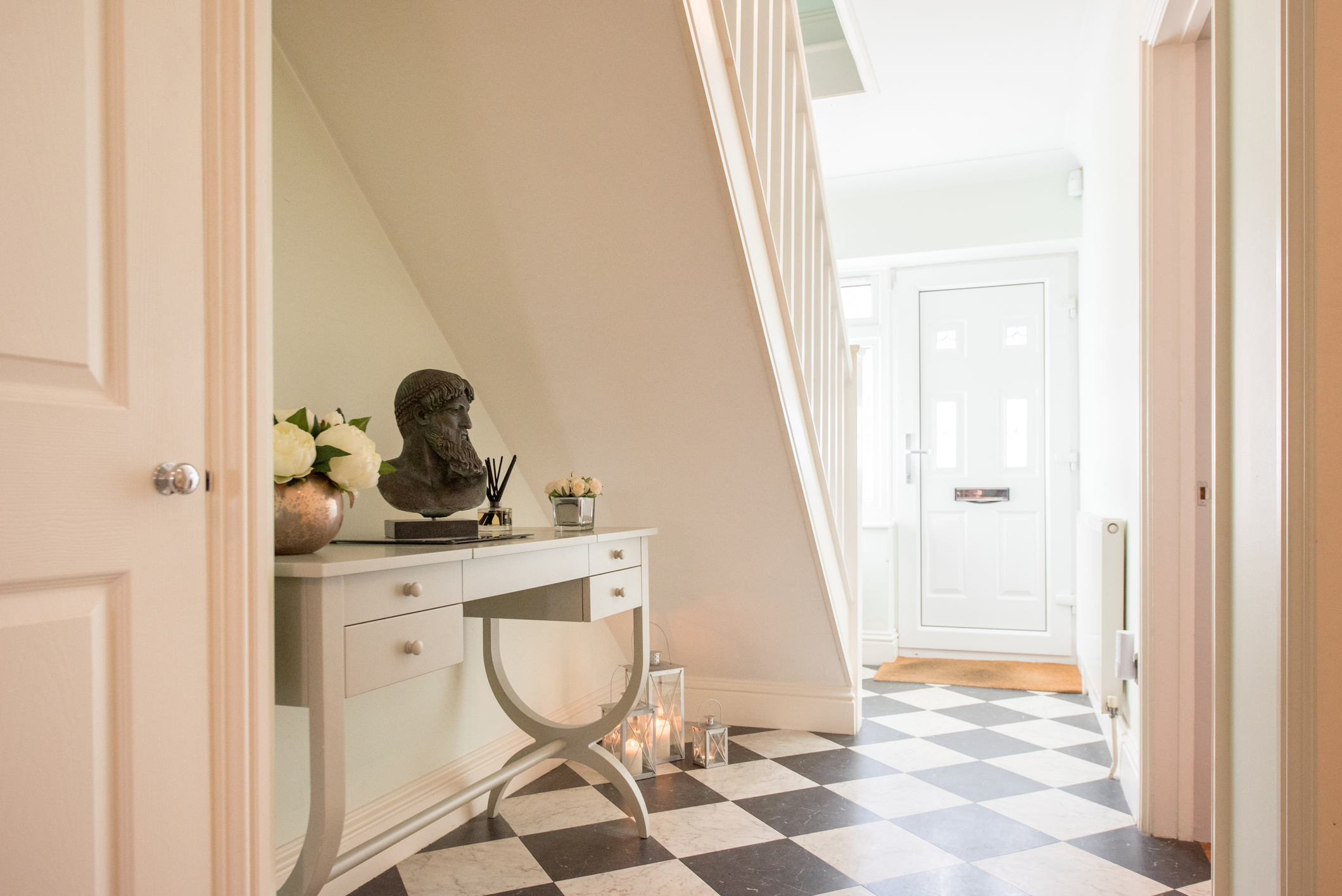 A hallway in a house with a checkerboard floor and a desk under the stairs. 