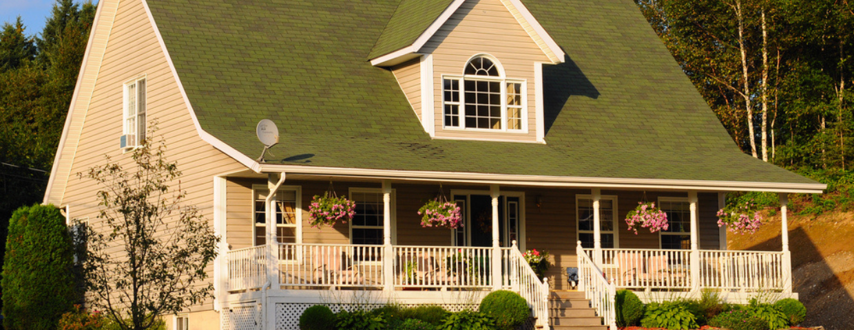 A Cottage style house with a low-pitched green roof and a large porch.