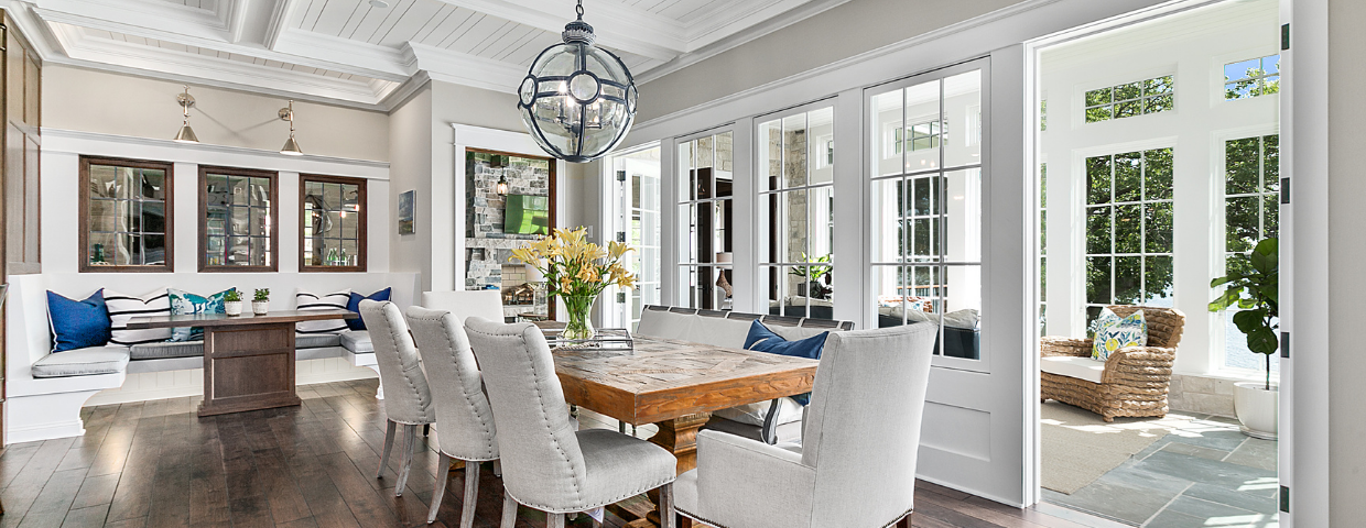 A dining room in a modern home with white chairs, hardwood floors, and windows surrounding the dining table.