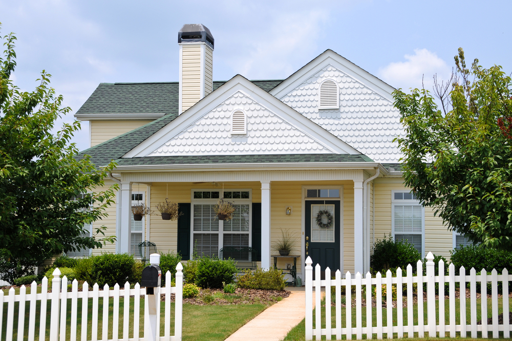 A yellow Cottage style house with a white picket fence in the front yard.