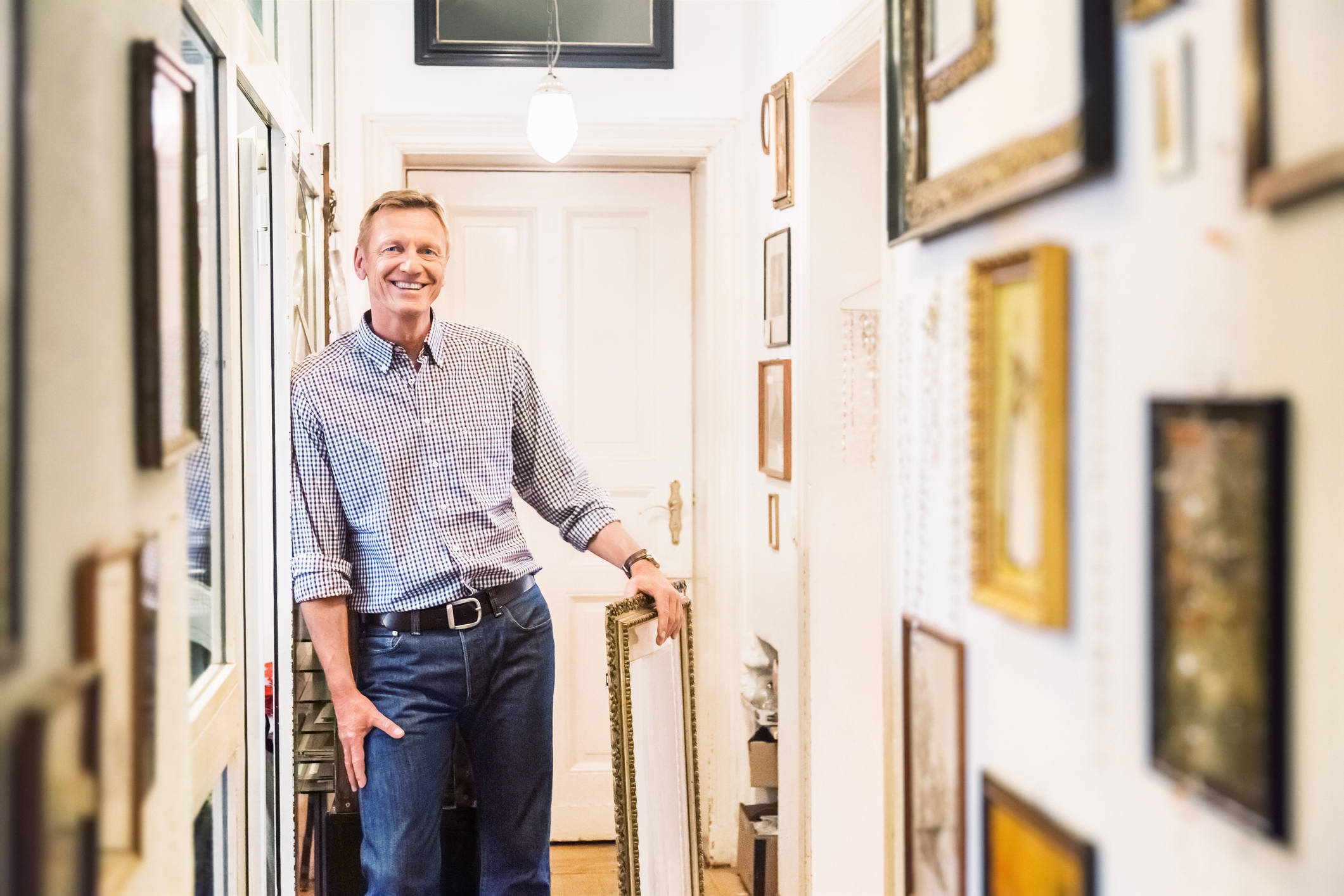 A man smiles standing in his hallway lined with framed photos.
