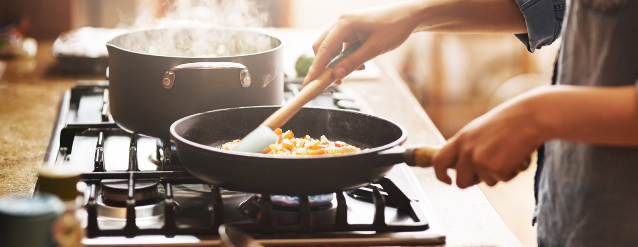 A close-up of a person’s hands cooking a meal on their kitchen stove.