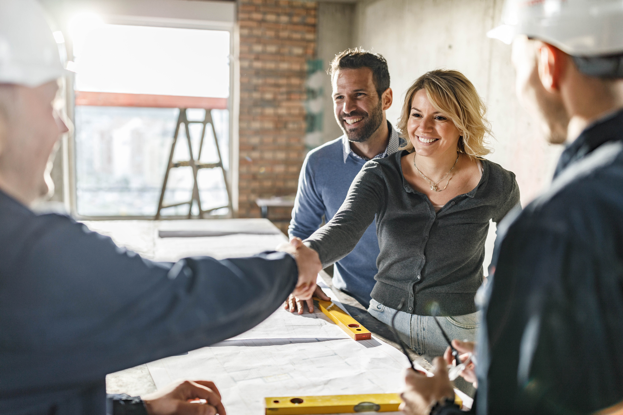 A man and a woman shake hands with two contractors as they go over their remodeling plans.