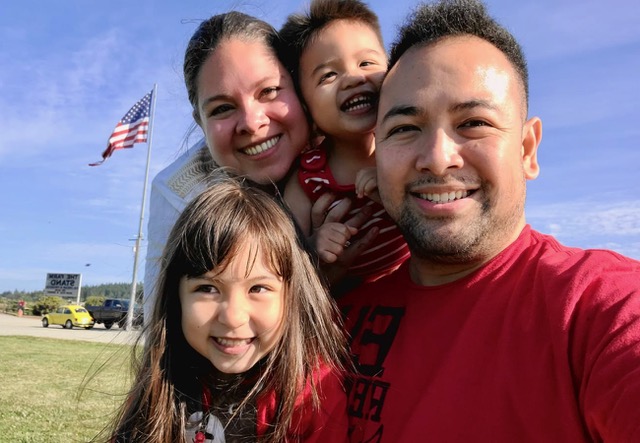 A selfie of a young man and woman and their two kids outside.