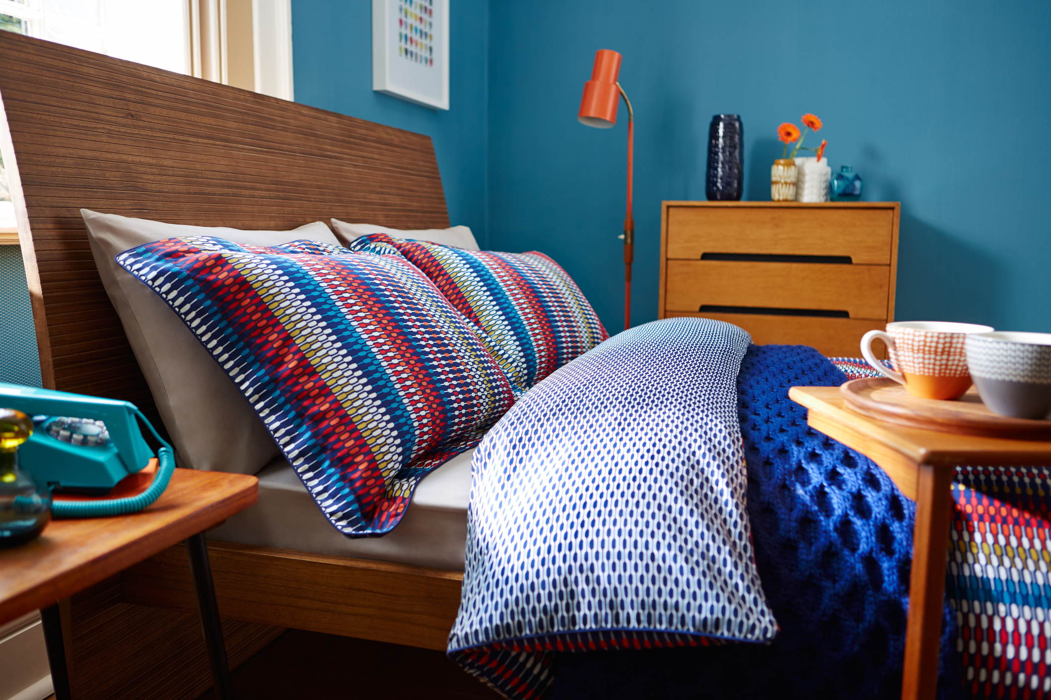 A colorful bedroom with blue walls, an orange lamp, and multicolored pillows and bedspread.