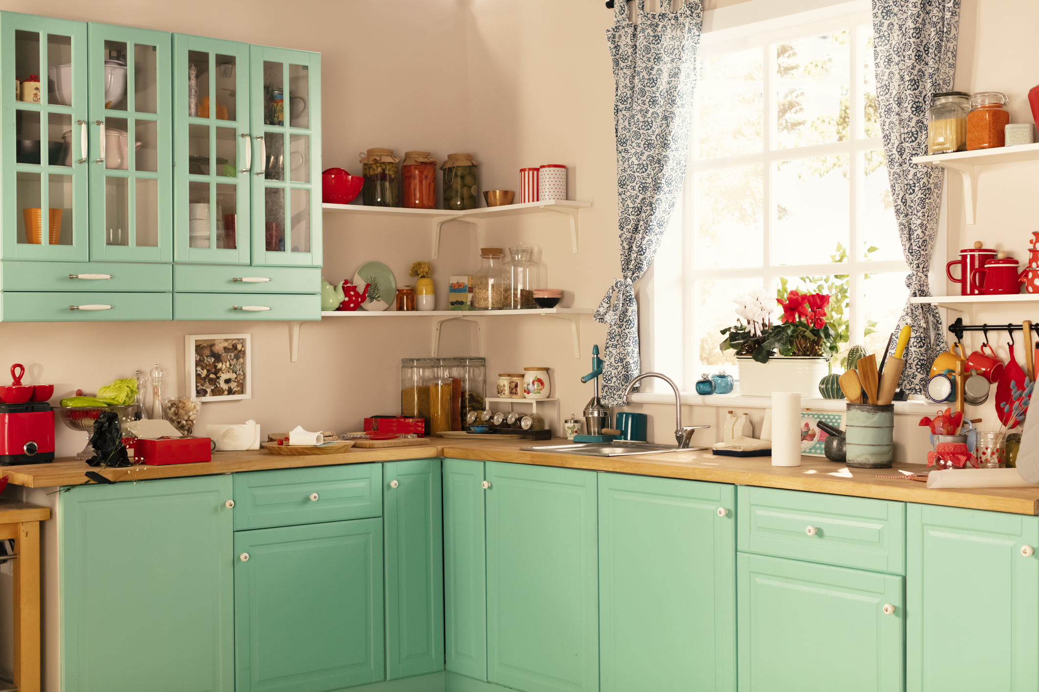 A colorful kitchen with mint green cabinets and red accents.