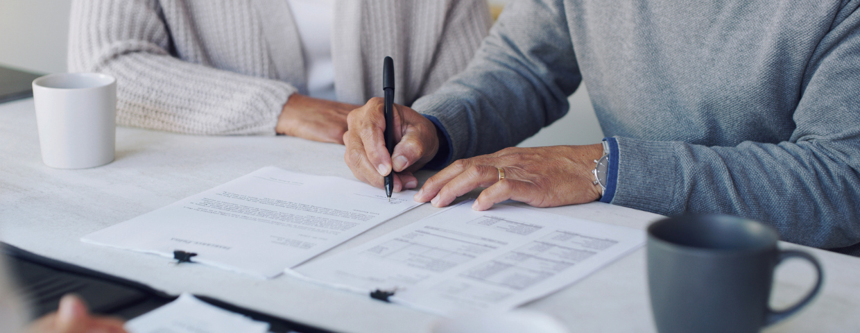 A close-up of a man and woman signing their escrow paperwork at a table.