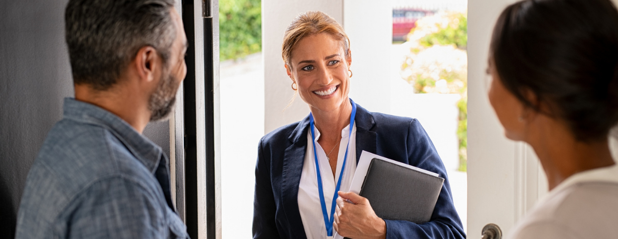 A real estate agent enters her clients’ home with a folder in her hands.