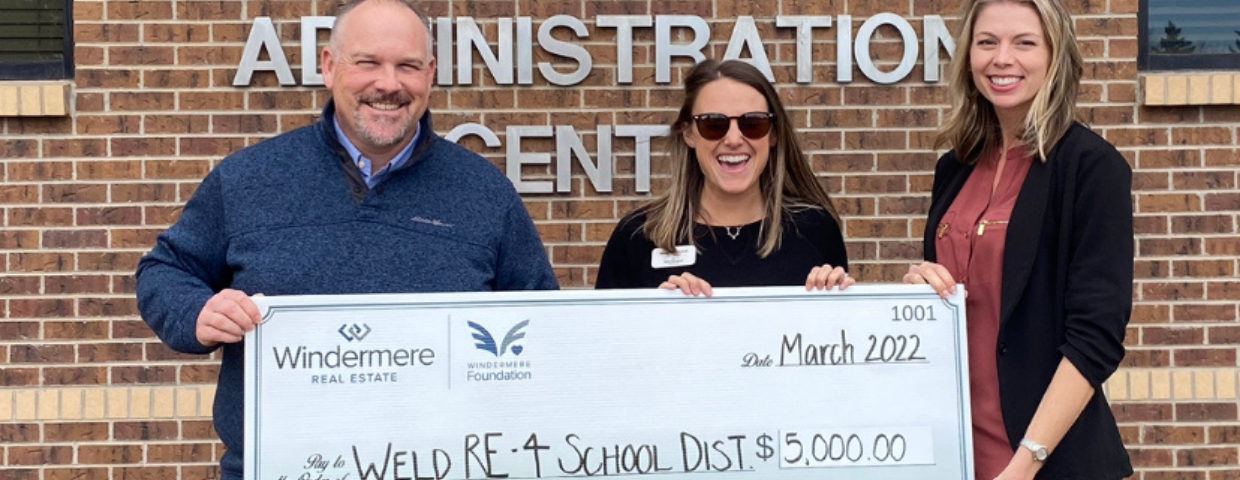 Two women and a man hold up a check for $5,000.