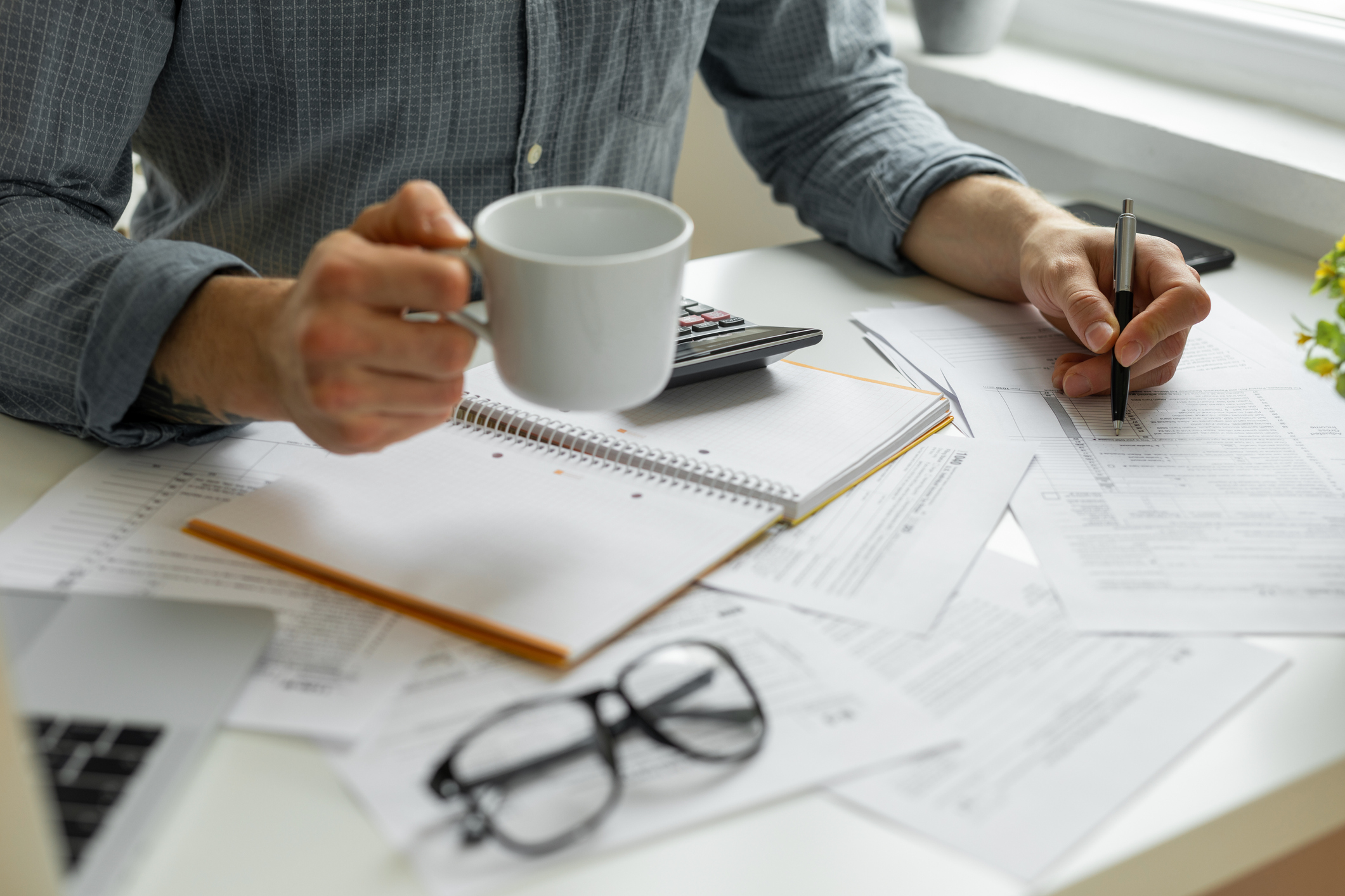 A young man drinks coffee while doing his taxes at home.