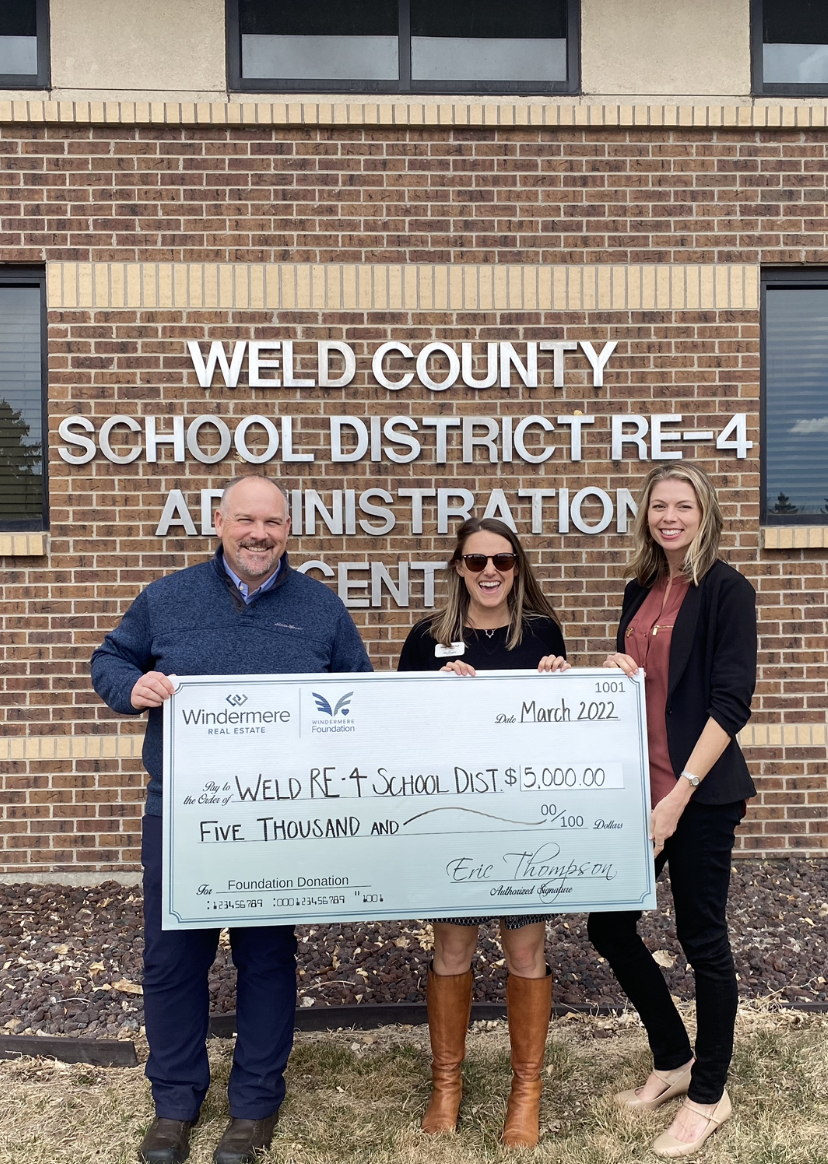 Two women and a man hold up a check for $5,000.