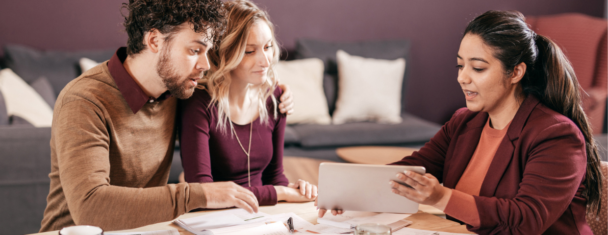 A young man and woman review financial paperwork with their real estate agent at a table