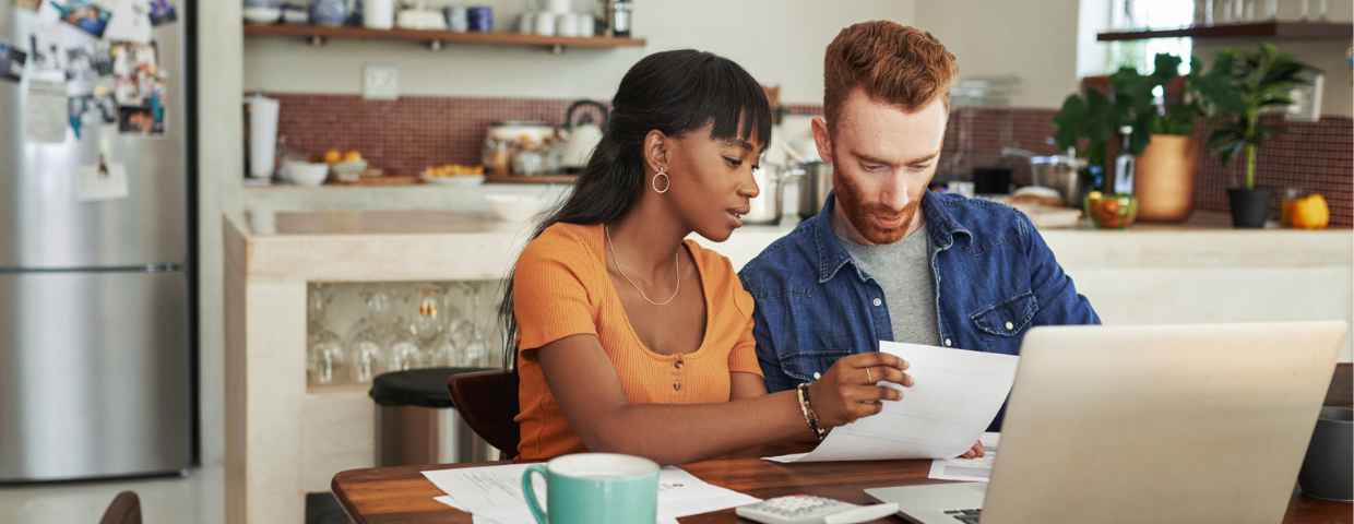 A young man and woman go over paperwork at their dining room table.