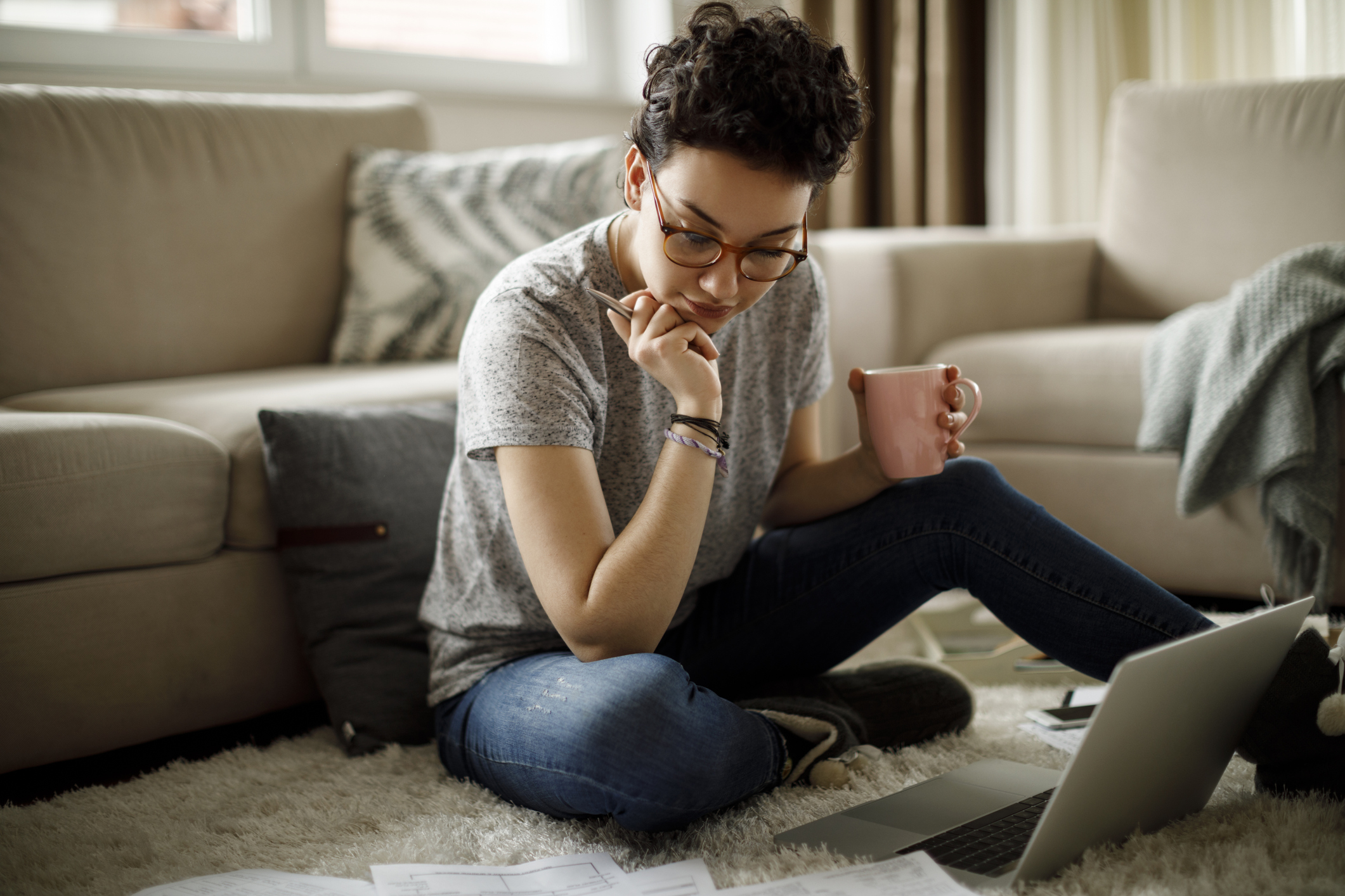 A young woman does paperwork on the floor of her living room.