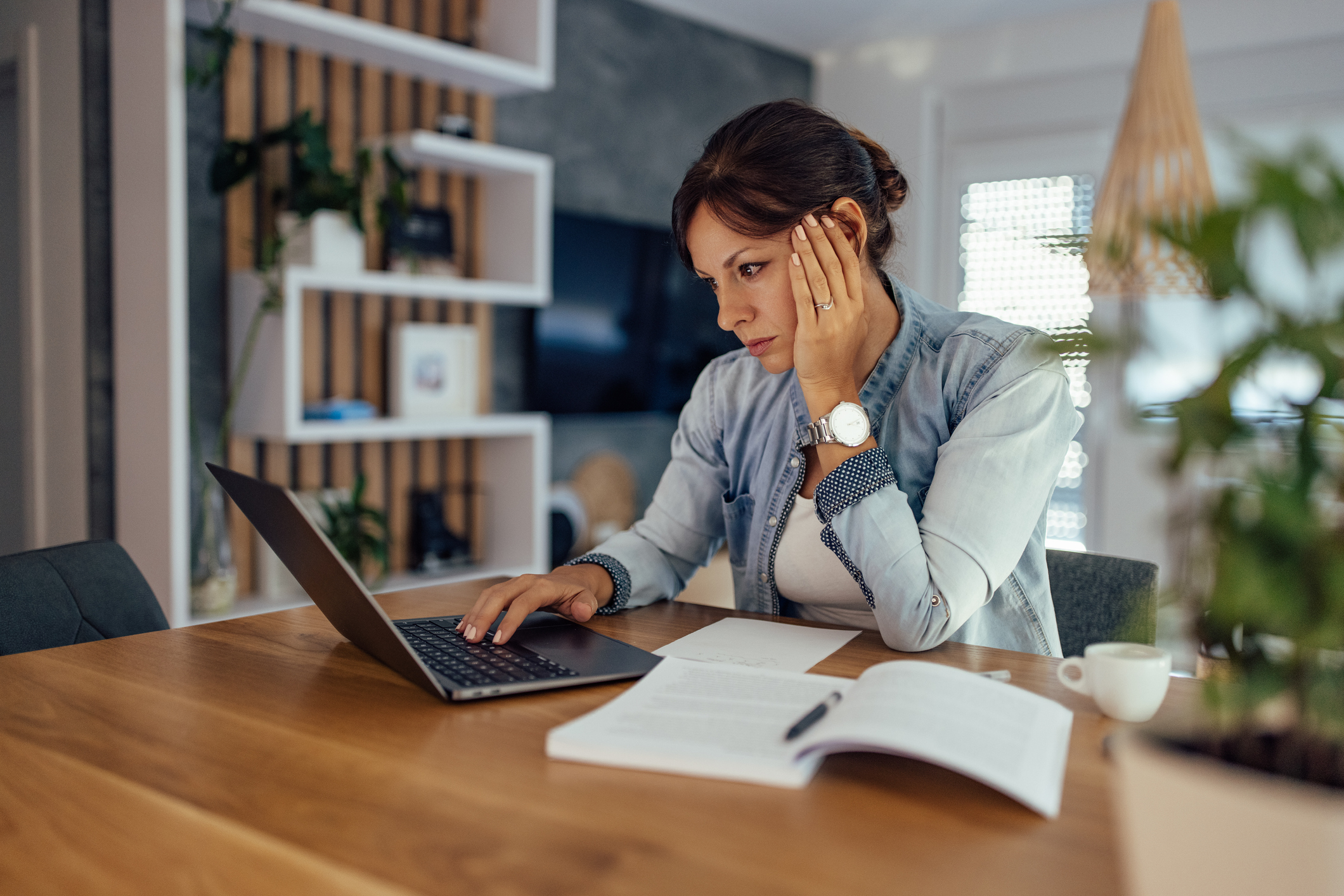 A woman does paperwork on her laptop at home.