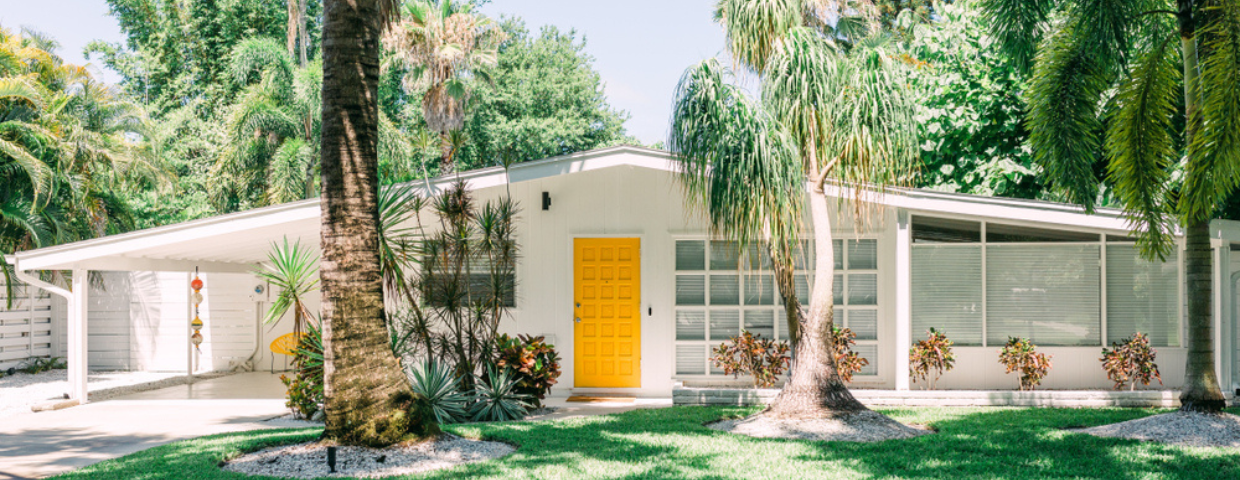 White mid-century modern house with large windows and a yellow door