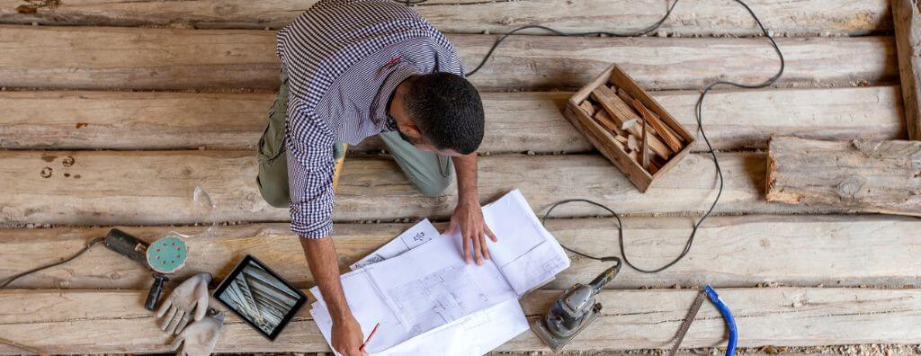 Birds-eye view of a homeowner looking at plans for his home DIY project with power tools around him