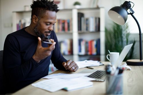 Man sitting at his computer at home talks to his real estate agent on the phone