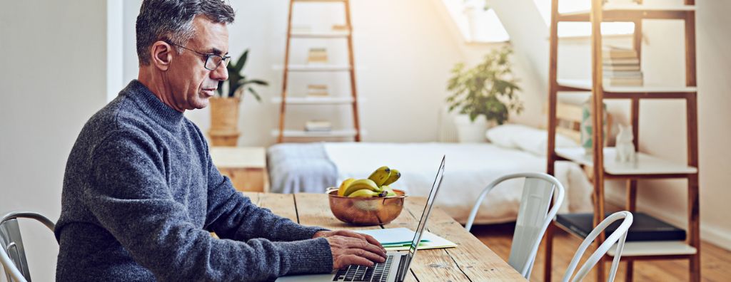 Man sitting at his computer at his dining room table researching the real estate market