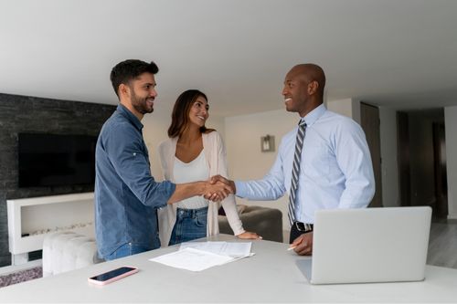 Man and a woman shaking hands with their real estate agent in the kitchen of their new home as they sign paperwork