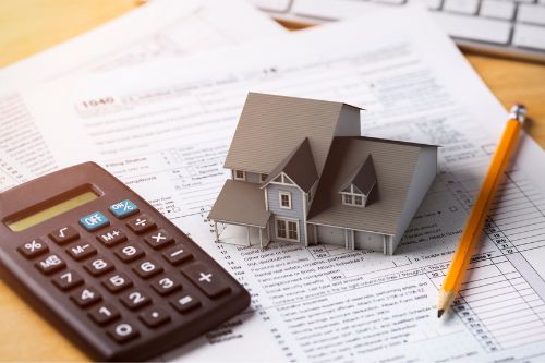 Overhead view of a miniature model house sitting on tax paperwork next to a calculator