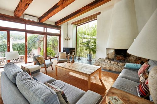 Modern farmhouse living room with a large grey couch, a coffee table, a fireplace, and big windows, with large wooden beams across the ceiling