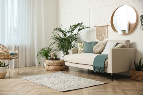 Comfortable chic living room with Traditional interior design style features, like neutral color pallet with wood and wicker accents, is expertly designed with large houseplants next to the couch