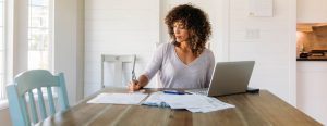 Woman in a bright house sitting at her dining room table completing financial paperwork