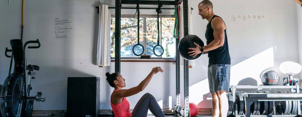 A young man and woman exercise together, passing a medicine ball back and forth in their home gym
